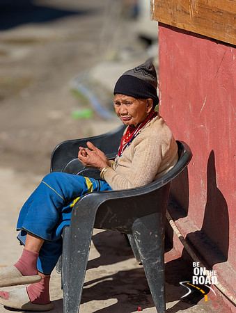 An elderly Arunachal Pradesh tribal women bathes in the morning sun outside of a restaurant